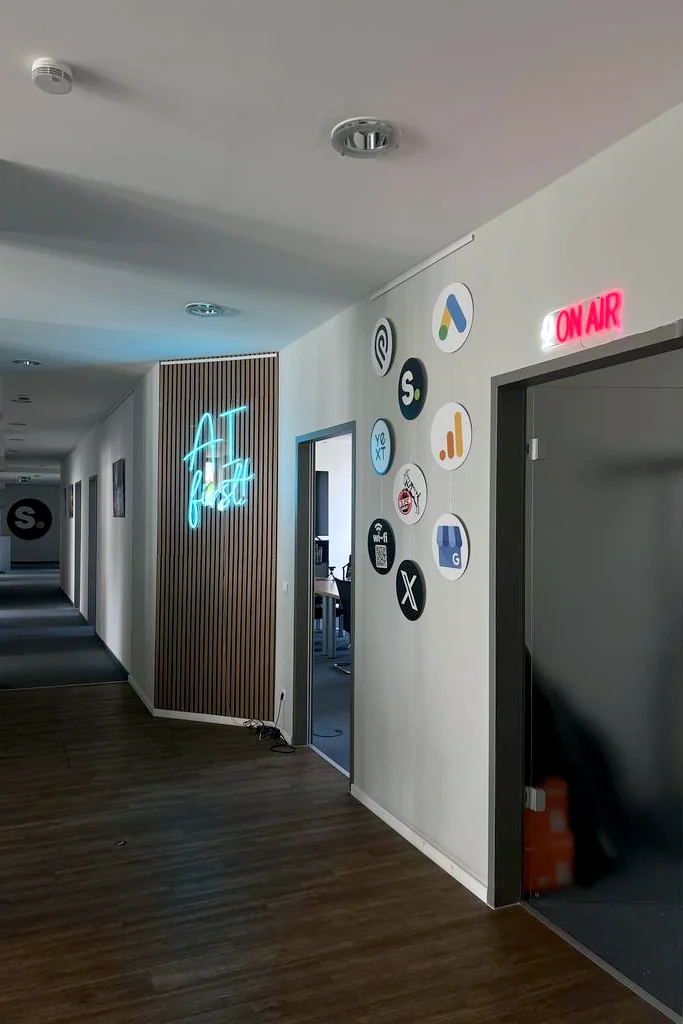 Bürogang von schmidtmedia mit Logowand, AI-first-Neonschild und leuchtendem ON-AIR-Schild