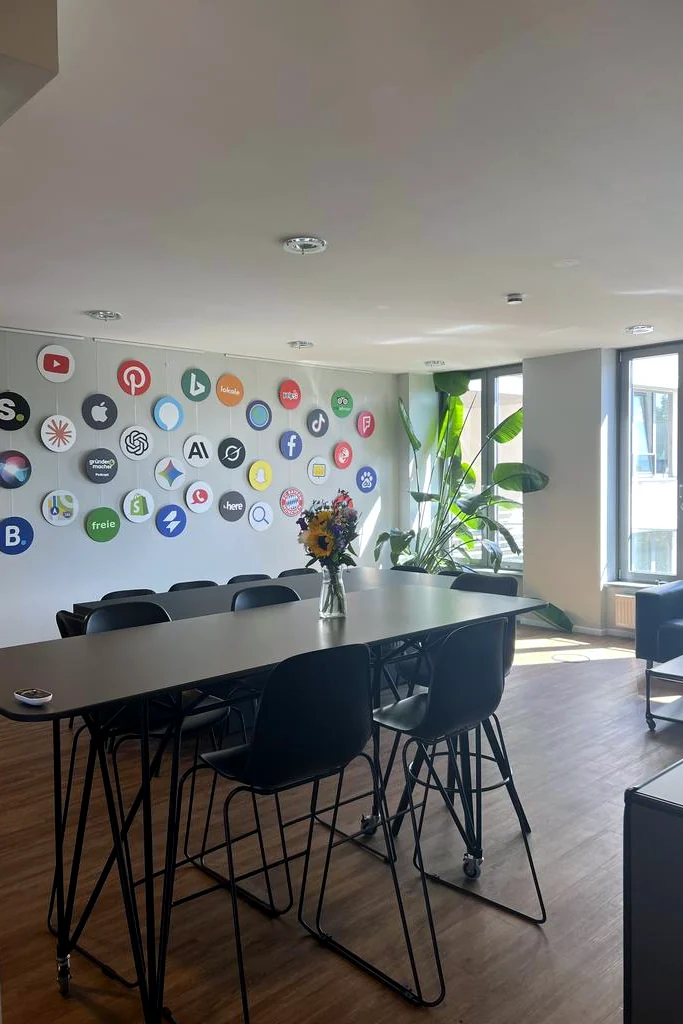 Meetingraum von schmidtmedia in Köln mit Logowand digitaler Plattformen und langem Besprechungstisch