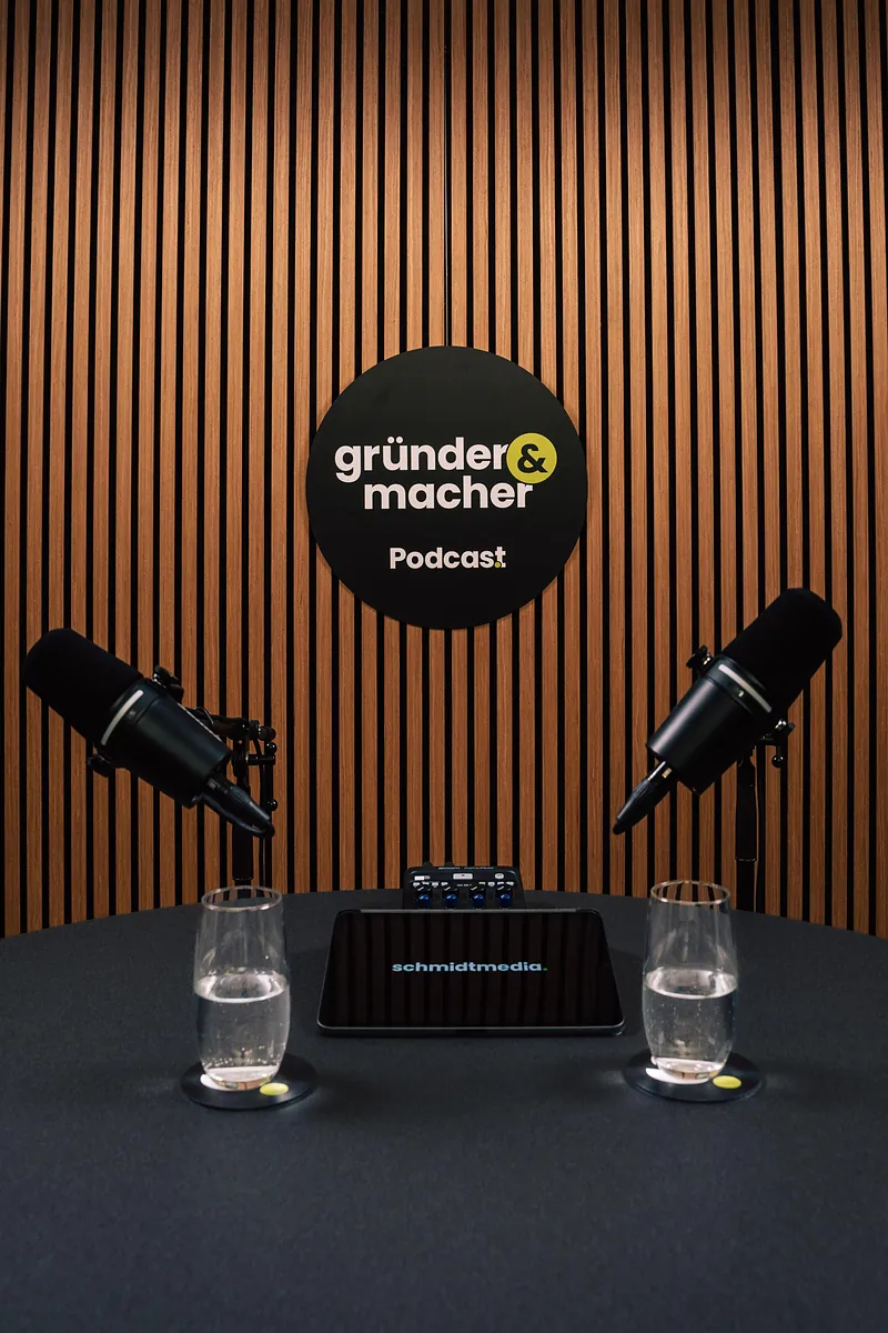 Podcast-Tisch von „gründer & macher“ mit zwei Mikrofonen vor der Holzlamellenwand im Studio von schmidtmedia in Köln