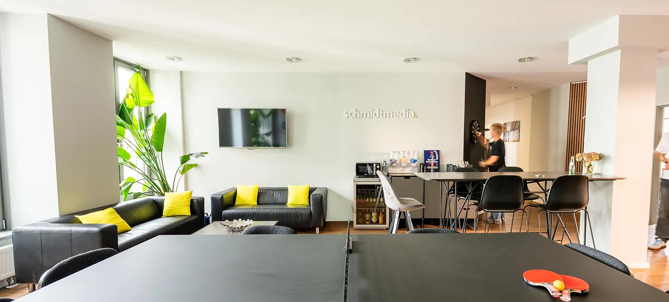 Offener Aufenthaltsbereich der Agentur schmidtmedia in Köln mit Lounge-Sofas, Küchenbar und Tischtennisplatte