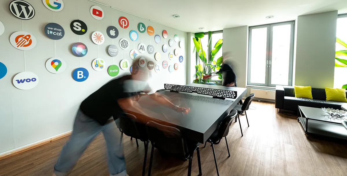 Arbeitsalltag bei schmidtmedia in Köln: Mitarbeiter in Bewegung vor der Wand mit Logos von WordPress, Google und Social-Media-Plattformen