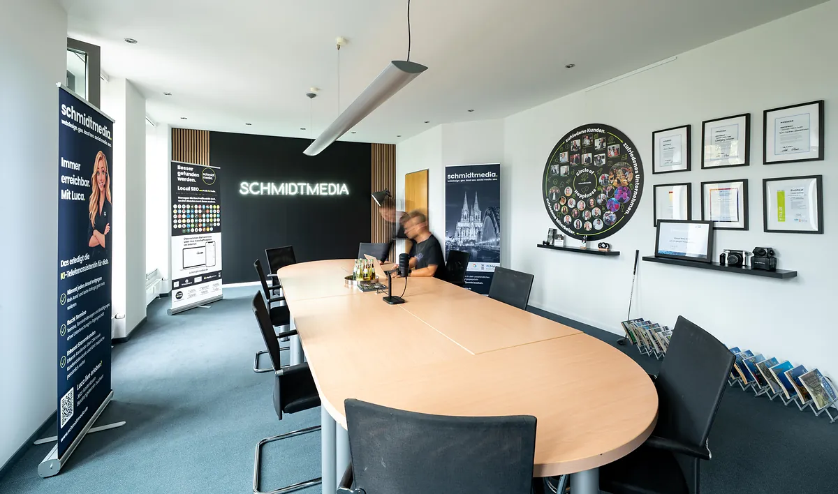 Besprechungsraum der Agentur schmidtmedia in Köln mit leuchtendem SCHMIDTMEDIA-Schriftzug und Auszeichnungen an der Wand