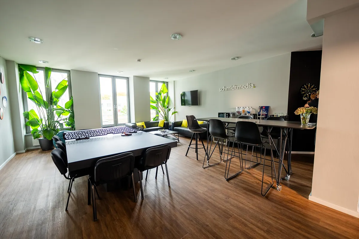 Heller Großraum im Büro der Agentur schmidtmedia in Köln mit Teamtischen, Pflanzen und Holzboden