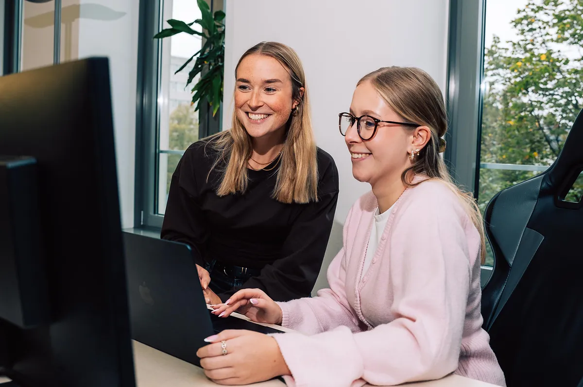 Zwei Kolleginnen der Online-Marketing-Agentur schmidtmedia arbeiten lachend gemeinsam am Laptop im Büro in Köln