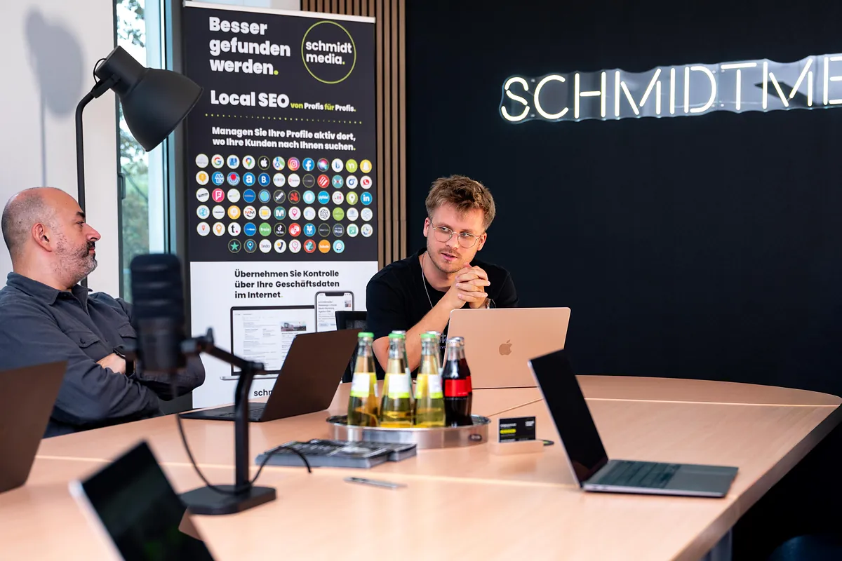 Kundengespräch bei schmidtmedia in Köln vor einem Local-SEO-Rollup und dem SCHMIDTMEDIA-Neonschriftzug