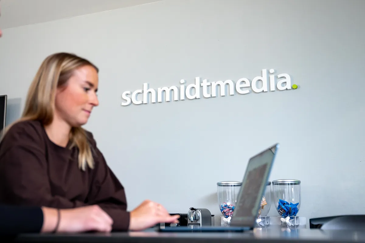 Mitarbeiterin von schmidtmedia arbeitet konzentriert am Laptop vor dem schmidtmedia-Logo im Büro in Köln
