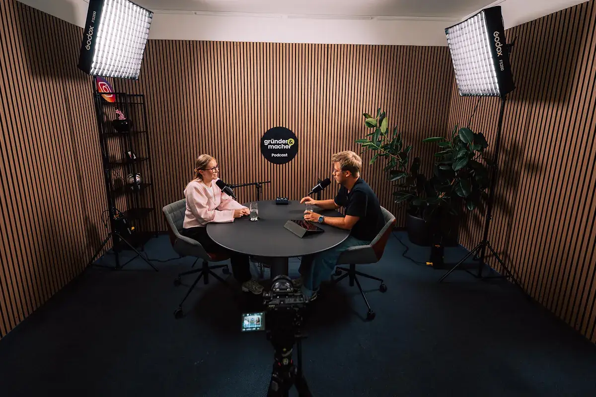 Weitwinkelblick ins Podcast-Studio von schmidtmedia in Köln mit Studioleuchten, Holzlamellenwand und Interview am runden Tisch